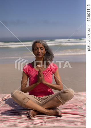 Senior woman with eyes closed and hands clasped doing yoga on beach 53001143