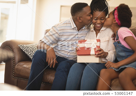 Happy African American father and daughter kissing mother on cheeks Happy African American father and daughter kissing mother on cheeks 53001147