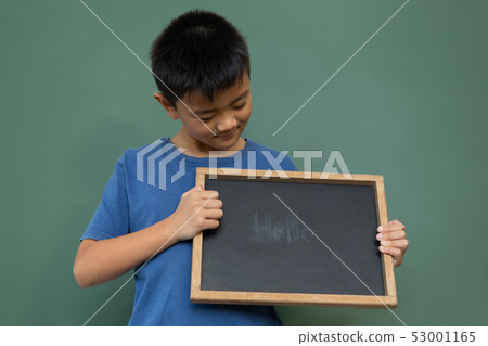 Smiling schoolboy standing and holding a hello slate in a classroom 53001165