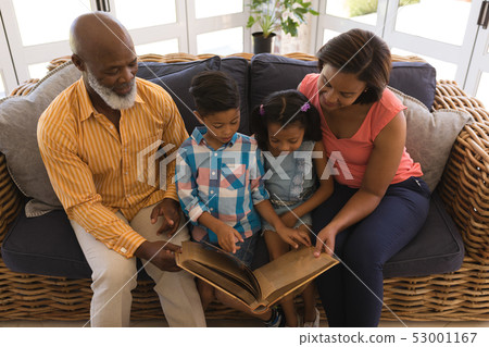 Multi-generation family reading a story book in living room 53001167