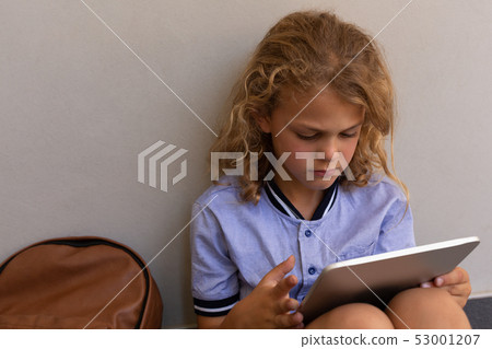 Schoolgirl with school bag sitting on the floor and using digital tablet Schoolgirl with school bag sitting on the floor and using digital tablet 53001207