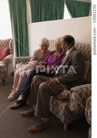 Front view of senior friends discussing over digital tablet while sitting on sofa Front view of senior friends discussing over digital tablet while sitting on sofa 53001250