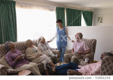 Female doctor interacting with senior people in living room 53001258