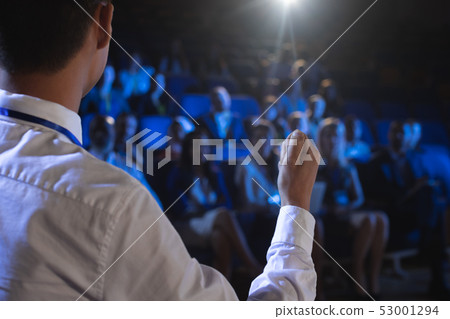 Businessman giving presentation in front of audience in auditorium Businessman giving presentation in front of audience in auditorium 53001294