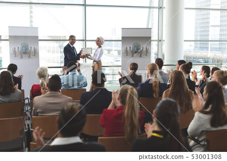 Businesswoman receiving award from businessman in a business seminar Businesswoman receiving award from businessman in a business seminar 53001308