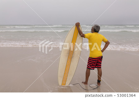 Senior male surfer standing with surfboard on the beach Senior male surfer standing with surfboard on the beach 53001364