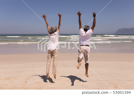 Senior couple with arms up jumping on beach Senior couple with arms up jumping on beach 53001394