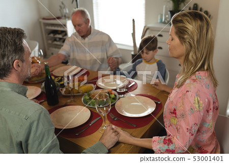 Family praying together before having meal on dining table Family praying together before having meal on dining table 53001401