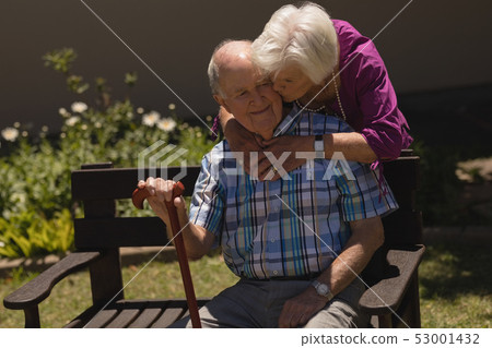 senior woman embracing and kissing senior man in garden 53001432