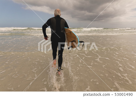 Senior man running with surfboard on the beach 53001490