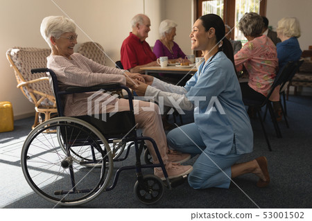 Side view of female doctor holding hands and talking with disable senior woman at home 53001502