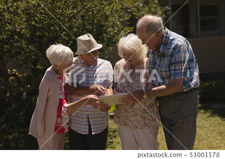 Front view of senior friends discussing over digital tablet in garden 53001578