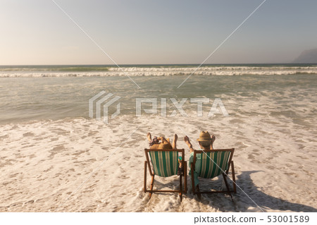 Senior couple relaxing together on sun lounger at beach 53001589