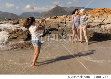 Little girl clicking photo of her family with mobile phone on beach Little girl clicking photo of her family with mobile phone on beach 53001713