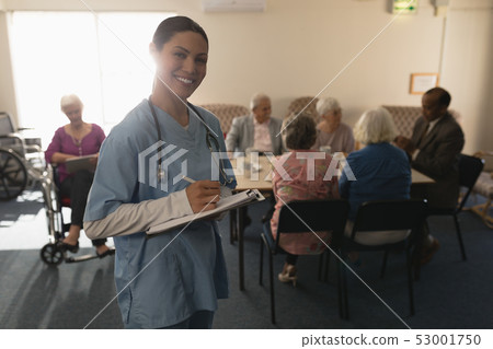 Front view of female doctor looking at camera while writing on clipboard at home Front view of female doctor looking at camera while writing on clipboard at home 53001750