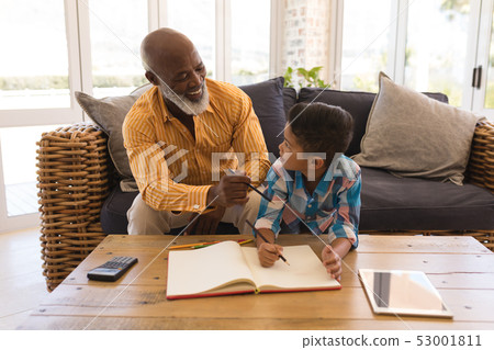 Grandfather helping his grandson with homework in living room 53001811
