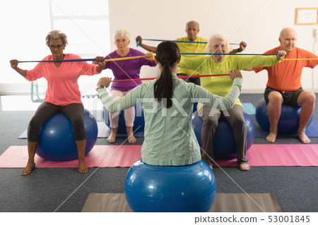 Young female trainer and senior people exercising with resistance band Young female trainer and senior people exercising with resistance band 53001845