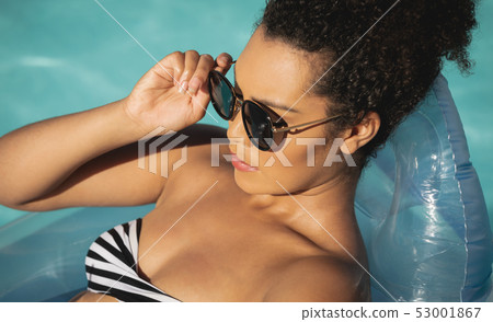 Young mixed-race woman with sunglasses relaxing on pool inflatable 53001867