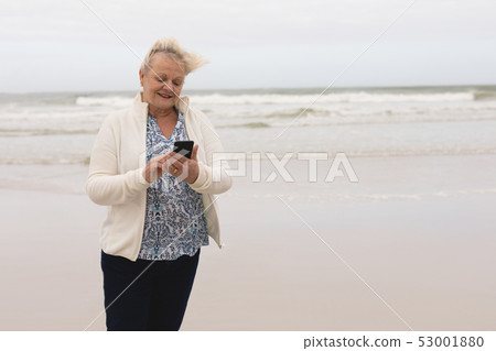 Happy senior woman using mobile phone standing at the beach Happy senior woman using mobile phone standing at the beach 53001880