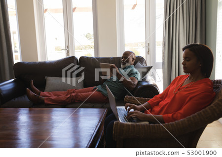 Senior woman using laptop while senior man using digital tablet in living room Senior woman using laptop while senior man using digital tablet in living room 53001900