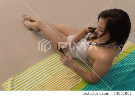 Young woman relaxing on blanket and using mobile phone Young woman relaxing on blanket and using mobile phone 53001901