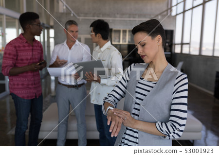 Female executive checking time on smartwatch in office Female executive checking time on smartwatch in office 53001923