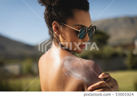 Young mixed-race woman rubbing sunscreen on shoulders 53001924