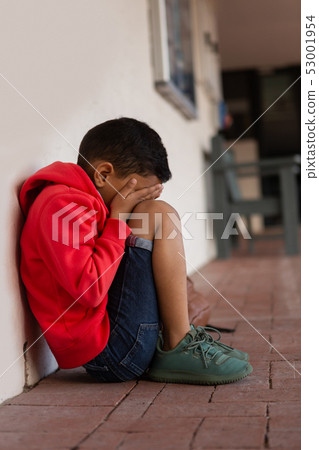 Sad schoolboy sitting alone on floor in corridor Sad schoolboy sitting alone on floor in corridor 53001954
