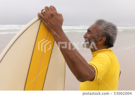 Senior male surfer standing with surfboard on the beach 53002004