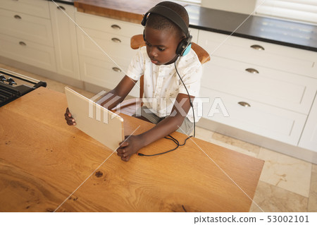 African American boy playing game on digital tablet at dining table in kitchen African American boy playing game on digital tablet at dining table in kitchen 53002101