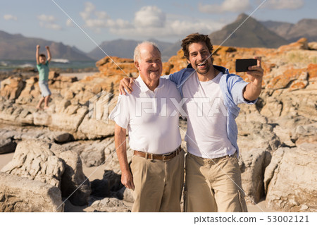 Happy father and son with arms around taking selfie with mobile phone Happy father and son with arms around taking selfie with mobile phone 53002121