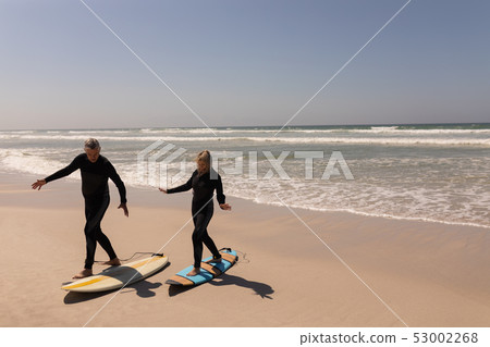 Side view of senior surfer couple walking on surfboard at beach 53002268