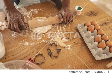 African American father and son rolling dough with rolling pin in kitchen 53002291