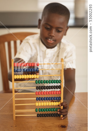 African American boy learning mathematics with abacus on dining table in kitchen 53002293