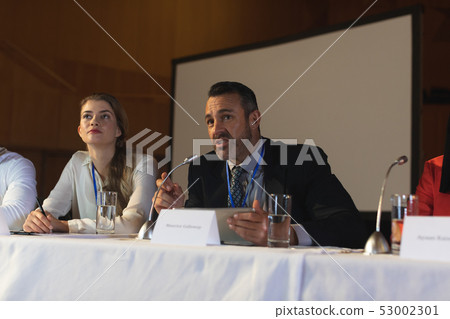 Businessman with executive speaking in speaker while sitting in the auditorium Businessman with executive speaking in speaker while sitting in the auditorium 53002301