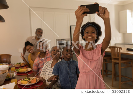 Girl taking selfie of family with mobile phone on dining table at home Girl taking selfie of family with mobile phone on dining table at home 53002338