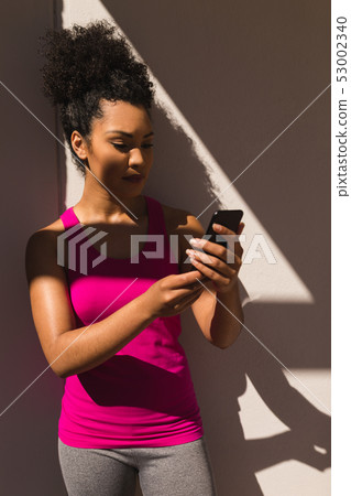 Woman wearing sportswear and using mobile phone in the backyard of home Woman wearing sportswear and using mobile phone in the backyard of home 53002340