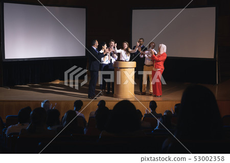Happy businesswoman standing at the stage of the auditorium with colleagues Happy businesswoman standing at the stage of the auditorium with colleagues 53002358