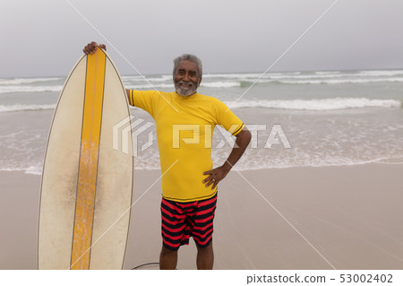 Senior male surfer standing with surfboard and looking at camera on the beach Senior male surfer standing with surfboard and looking at camera on the beach 53002402