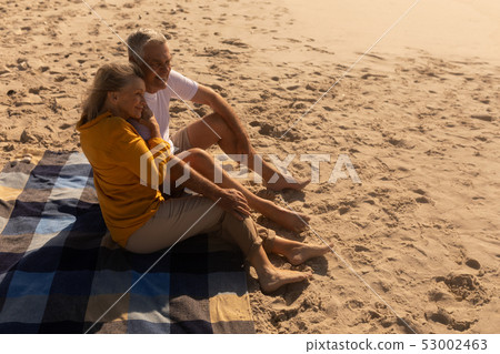 Senior couple relaxing on picnic blanket at beach 53002463