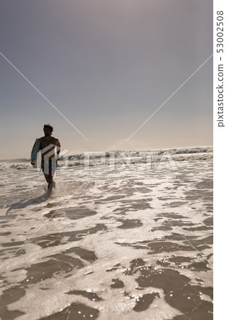 Young male surfer with surfboard running on beach Young male surfer with surfboard running on beach 53002508