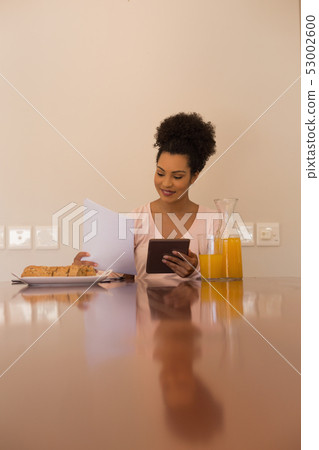 Woman looking at form while using digital tablet at home Woman looking at form while using digital tablet at home 53002600