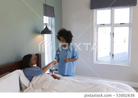 Female doctor giving medicine to senior woman in bedroom 53002636
