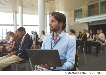 Young businessman with laptop looking away during seminar 53002870