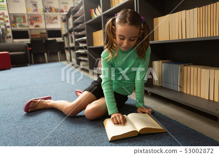 Schoolgirl sitting on floor and reading a book in library Schoolgirl sitting on floor and reading a book in library 53002872