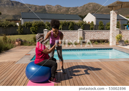 Female trainer training senior woman in performing exercise in the backyard Female trainer training senior woman in performing exercise in the backyard 53002896