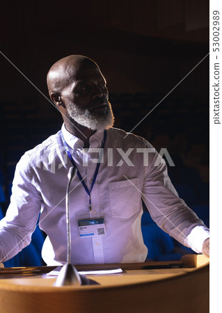 Businessman looking and thinking while standing on stage in auditorium 53002989
