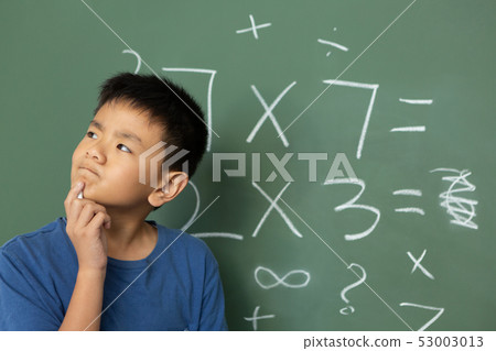 Thoughtful schoolboy doing math on green chalkboard in a classroom Thoughtful schoolboy doing math on green chalkboard in a classroom 53003013