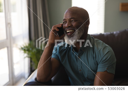 Senior man talking on mobile phone in living room Senior man talking on mobile phone in living room 53003026