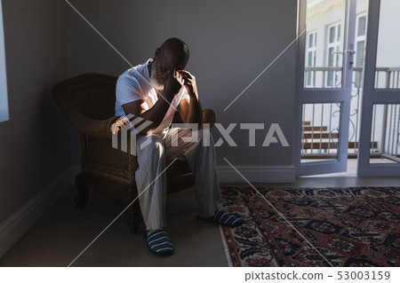 Worried senior man sitting on wicker chair in living room Worried senior man sitting on wicker chair in living room 53003159